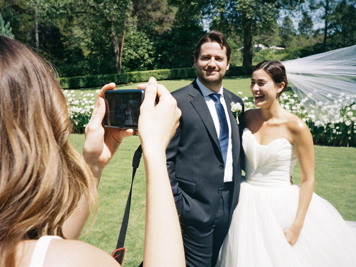 A wedding photographer with a couple on a bright lawn