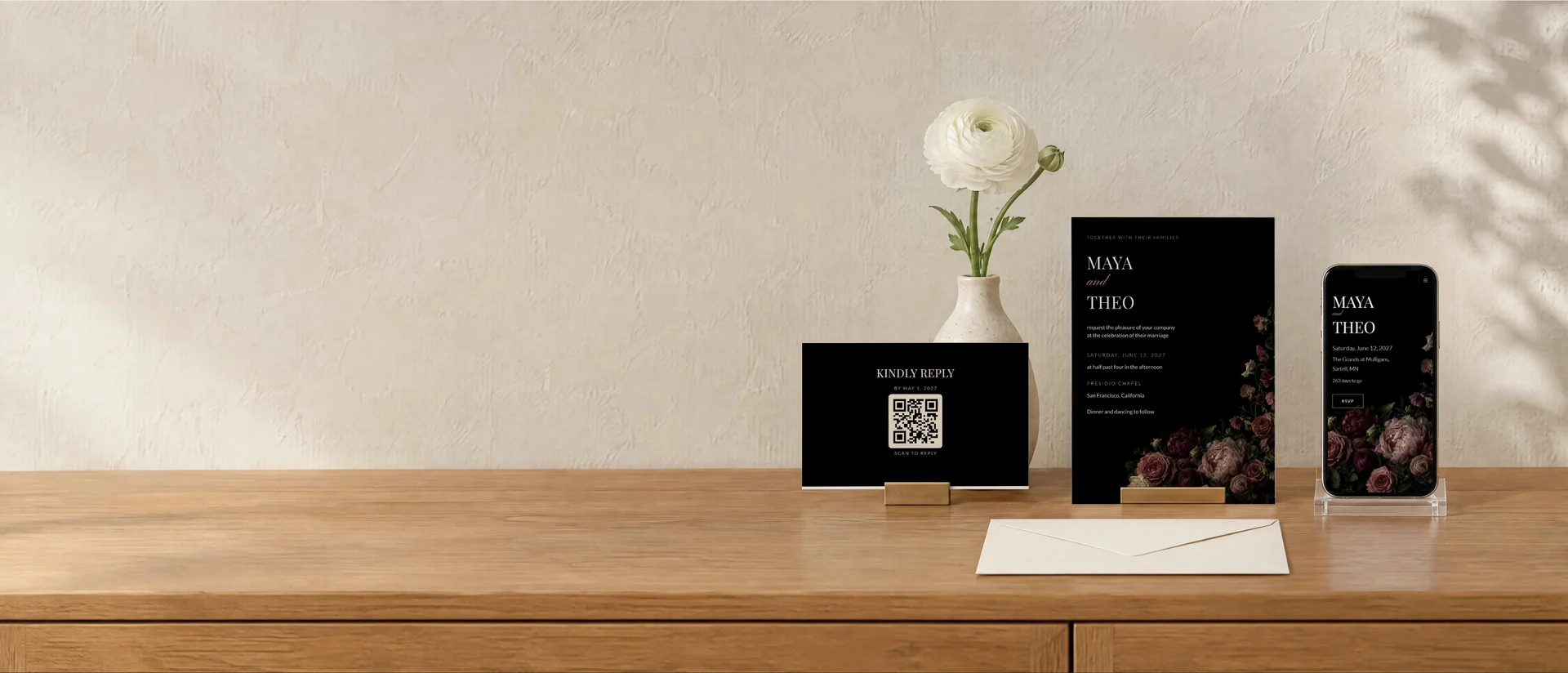An invitation and a reply card in brass holders on an oak sideboard, beside a phone showing the same design as a wedding website